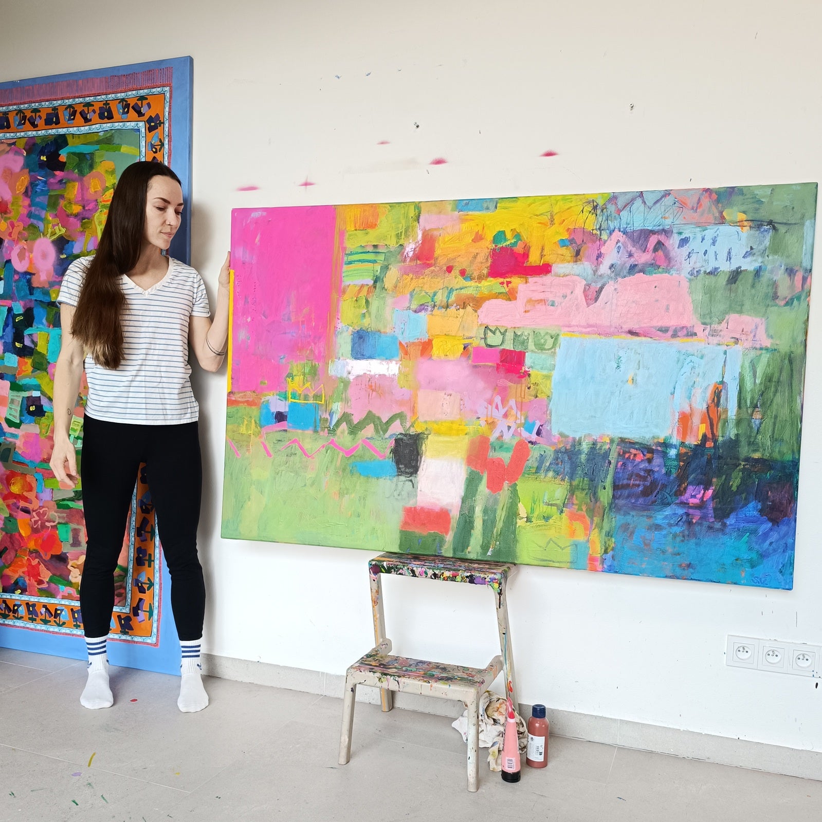 Artist standing next to large abstract painting in contemporary art studio with textured canvas artwork